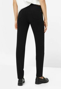 Pantalones ajustados negros con una textura suave, que cuentan con dos bolsillos traseros y una cintura de altura media. Llevados con mocasines negros.