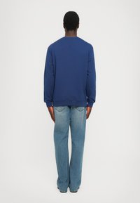 Sudadera azul marino con mangas largas, cuello redondo y puños acanalados; combinada con unos pantalones vaqueros de pierna ancha en azul claro y zapatos negros.