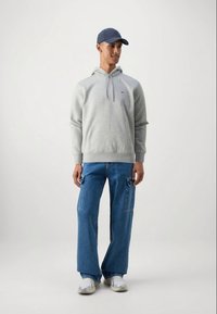 Grå hættetrøje med en kængurulomme, parret med lyseblå brede denim cargo bukser. Hvide og grå sneakers fuldender outfittet. Blå kasket bæres.