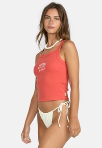 Top sin mangas de canalé color coral con un logo blanco, combinado con una parte de abajo de bikini blanca de textura que presenta lazos en los laterales. Tejido suave, diseño entallado.