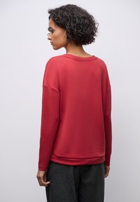 Rød sweatshirt med lange ærmer, rund halsudskæring, afslappet pasform og ribbede manchetter. Glat tekstur, vist fra bagsiden mod en ensfarvet baggrund.