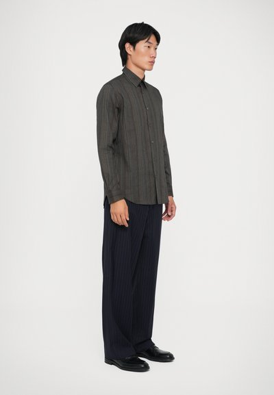 Camisa abotonada con rayas verticales multicolores, de manga larga y cuello plano; combinada con pantalones anchos a rayas y zapatos negros.
