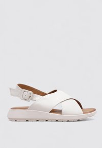 Sandaña de cuero blanco con diseño de tiras cruzadas, hebilla ajustable en el tobillo, suela de goma y plantilla marrón para comodidad y soporte.