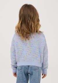 Jasnoniebieski sweter dziany z teksturowanym wzorem, z pastelowymi plamkami. Ściągacze przy mankietach i u dołu, noszony z dżinsami wysokiego stanu.