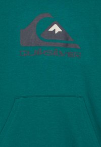 Sweatshirt vert avec un grand logo Quiksilver gris foncé, présentant un design de montagne et de vagues, et une poche avant en bas.