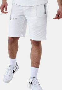 Bermudas deportivas blancas fabricadas en un tejido suave, con dos bolsillos laterales, uno de ellos con un acento de marca, y un corte recto hasta la rodilla.