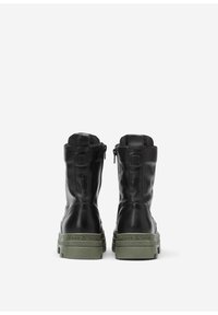 Zwarte leren enkelboots met een groene rubberen zool, voorzien van een ritssluiting en textuuraccenten aan de achterkant.