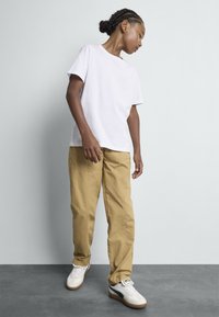 T-shirt en coton blanc et pantalon cargo beige clair. La tenue est accompagnée de baskets blanches avec un accent noir et une semelle texturée.