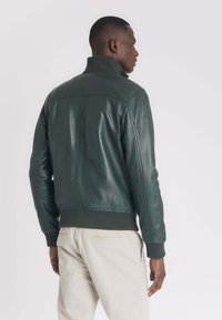 Groene leren jas met een hoge kraag, geribbelde manchetten en onderrand, met een gladde textuur en een getailleerde pasvorm. Subtiele stiknaaddetails aan de achterkant.