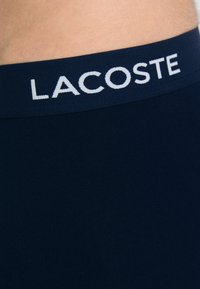 Navy blue waistband with white "LACOSTE" logo; smooth texture and elastic material typical of men's underwear.