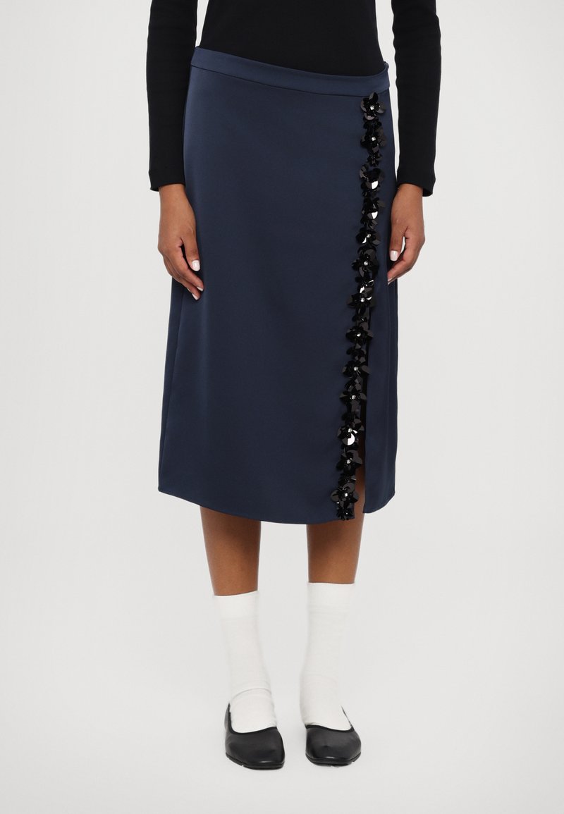 Jūras laivu zilās midi svārki ar taisnu griezumu, dekorēti ar melnām sekvīnu ziedu akcentiem kreisajā pusē un delikātu sānu šķēlumu.