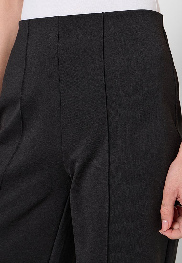 Czarne spodnie z wysokim stanem, wykonane z teksturowanej tkaniny, z trzema pionowymi plisami z przodu i gładkim wykończeniem. Brak widocznych kieszeni.