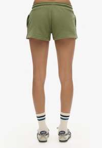 Pantalones cortos de algodón en verde oliva con una cintura elástica y bolsillos laterales, combinados con calcetines blancos con rayas azules y sandalias grises.