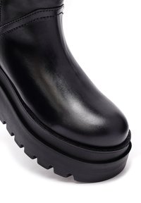 Czarne skórzane botki za kostkę z błyszczącym wykończeniem, masywną podeszwą platformową i zaokrąglonym noskiem. Widoczne szwy wzdłuż boków.