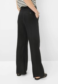 Wide-leg black pants in a textured fabric, featuring side pockets, a sleek waistband, and a subtle brand tag at the back.
