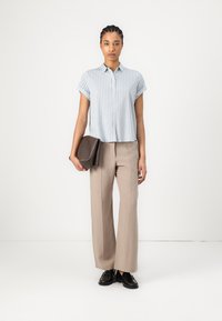 Camicia a maniche corte a righe blu, pantaloni beige a gamba larga e scarpe nere, abbinati a una clutch marrone scuro. Aspetto moderno e pulito.