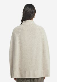 Beige stickad sjal med hög krage, ribbat avslut och texturerat mönster. Har en lös passform och mjukt, mysigt material.