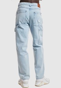 Lyseblå denim cargo bukser med avslappet passform, flere lommer og en subtil logo merkelapp på bakre livlinje. Gummi detaljer på lommene.