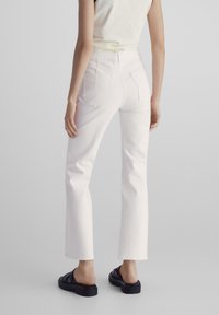 Witte denim broek met een rechte snit, vijf zakken en subtiele stiksels. Gekozen in combinatie met zwarte casual sandalen, wat een schone, minimalistische uitstraling geeft.