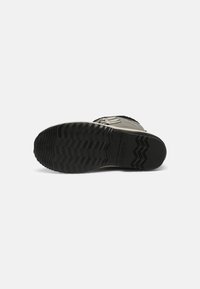 Suela de goma negra con un patrón de agarre texturizado y acentos en zigzag; parte superior de tela gris con detalles de cordones y logotipo.