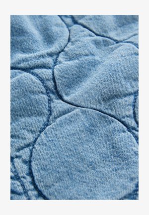 Denimstof med en quiltet design og cirkulære mønstre; lyseblå farve, blød tekstur og synlige syninger.