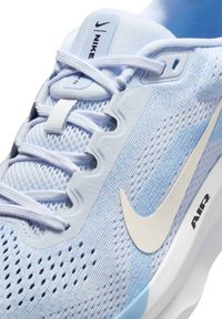 Scarpa atletica azzurro chiaro con tomaia in rete, dettagli bianchi e logo Nike. Presenta una superficie texturizzata e un design con lacci tradizionale.