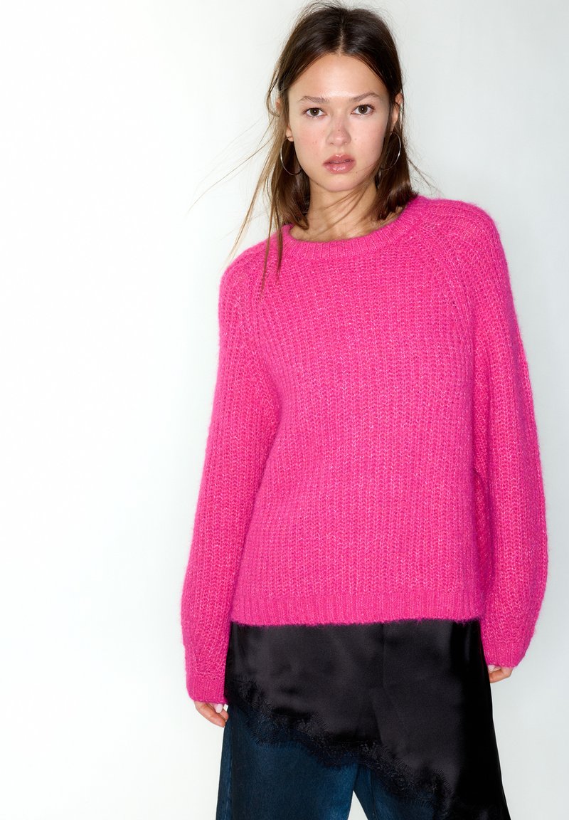 Pull tricoté fuchsia à coupe ample, col rond et motif texturé. Superposé à un top en satin noir orné de détails en dentelle.