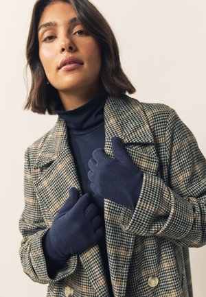 Granatowe rękawiczki z polaru o miękkiej fakturze i otworami na palce, noszone przez osobę w kratkowanym płaszczu na ciemnym golfie.