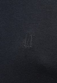 Pulover tricotat negru, cu un logo texturat subtil embosat pe țesătură, oferind un design curat și minimalist.