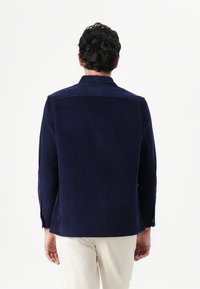 Chaqueta de pana navy con cuello, mangas largas y rayas verticales texturizadas; cuenta con puños abotonados y dobladillo recto.