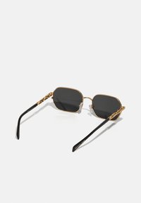 Goldfarbene, metallische, achteckige Sonnenbrille mit schwarzen Gläsern, die an den Bügeln strukturierte goldene Akzente sowie schwarze Kunststoff-Enden an den Bügeln aufweist.