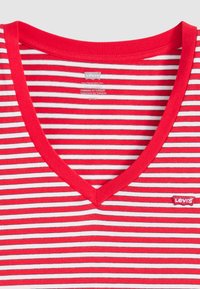 T-shirt rayé rouge et blanc avec un design en V, étiquette de logo Levis, en coton doux et à coupe décontractée.
