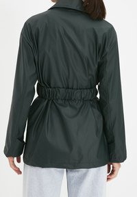 Dark green, lightweight jacket with a cinched waist, long sleeves, and a collared neckline, made of smooth, water-resistant material.