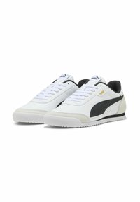 Baskets en cuir blanc avec une bande en suède noire, dotées d'une semelle texturée, d'un design à lacets et d'un col rembourré. Accent du logo doré sur le côté.