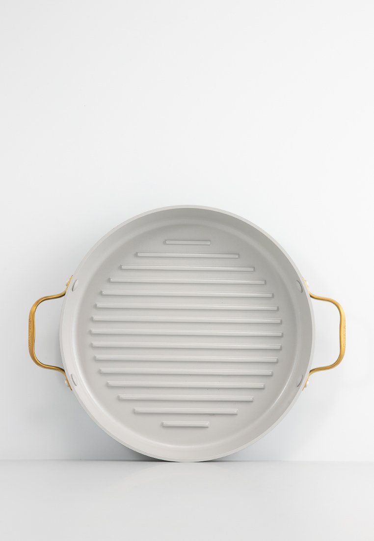 Poêle grill ronde grise avec des bords surélevés et des poignées dorées des deux côtés, sur fond blanc.
