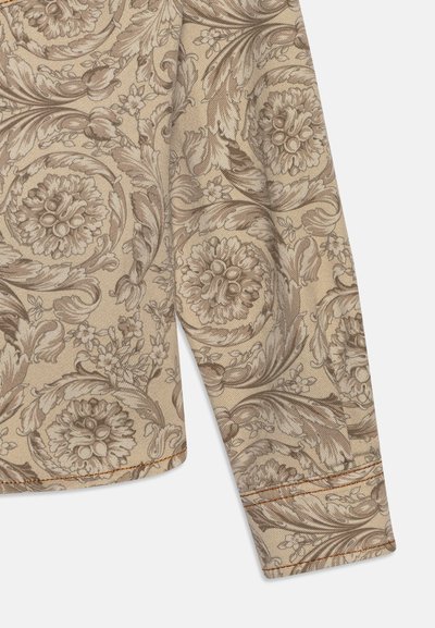 Tessuto beige con intricati motivi floreali marroni, caratterizzato da dettagli testurizzati. Il bordo presenta cuciture visibili in una tonalità di contrasto.