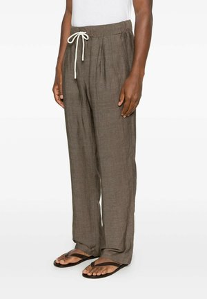 Persona che indossa pantaloni larghi di lino marrone con coulisse e infradito nere, in piedi con le mani rilassate lungo i fianchi.