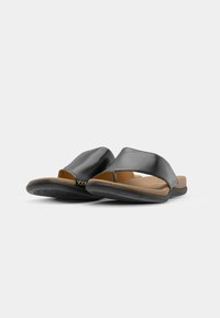Sandales à glisser en cuir noir avec un bout ouvert, semelle en tan et semelle en caoutchouc texturé. Présente un accent en couture croisée sur la lanière supérieure.