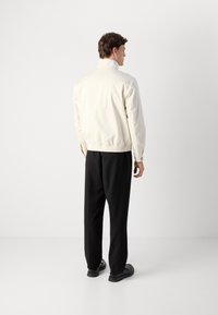 Cream bomber jacket with elastic hem and cuffs, paired with black trousers and black shoes. Smooth texture, minimal design, no visible logos.