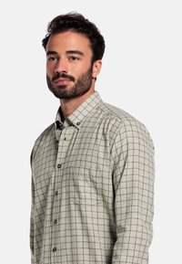 Groen en beige geruite blouse met lange mouwen, knoopsluiting aan de voorkant, borstzak en een zachte textuur. Heeft donkere knopen en een kraag.