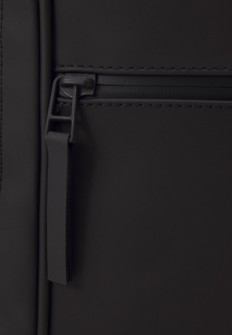 Detail van een zwarte nylon tas met ritsluiting, een soepele textuur en een flexibele rits. Subtiele stiksels langs de randen.