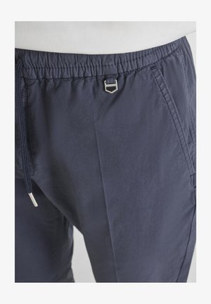 Pantaloni con vita elasticizzata blu navy, tasche frontali, coulisse e piccolo dettaglio decorativo in metallo argento al centro della vita.