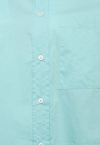 Camicia button-up azzurro chiaro realizzata in cotone morbido, con taschino sul petto, bottoni bianchi e una texture sottile. Design con colletto classico.