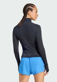 Μαύρη αθλητική μπλούζα με μακριά μανίκια, στενή εφαρμογή και υφή, συνδυασμένη με ελαφριά μπλε σορτσάκια με χωριστό μπατζάκι.