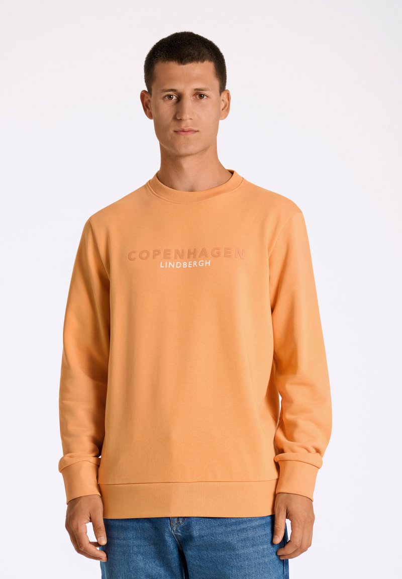 Felpa arancione con collo rotondo e polsini a costine. Presenta una stampa del testo "COPENHAGEN" e "LINDBERGH" in un colore a contrasto. Texture morbida.