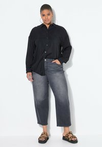 Czarna koszula zapinana na guziki z długimi rękawami, zestawiona z szerokimi ciemnoszarymi dżinsami. Uzupełniona sandałami w panterkę i dużymi kolczykami w kształcie kół.