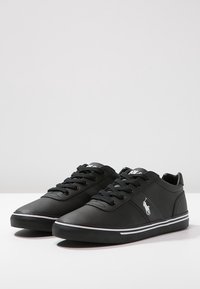 Svarta snörskor i lace-up stil, gjorda av slätt syntetiskt material med låg klackdesign, med vita detaljer och en liten logotyp på sidan.