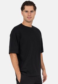 T-shirt en coton noir avec manches courtes, col rond et coupe décontractée. Texture lisse sans motifs ni accents visibles.