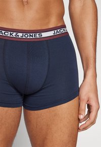 Marineblaue Baumwollboxershorts mit einem burgunderrot-weißen Elastikbund, der den Markennamen "JACK & JONES" trägt. Glatte Textur, körperbetontes Design.