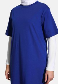 Modré bavlněné tričko, krátké rukávy, kulatý výstřih, volný střih, vrstvené přes dlouhé bílé tričko s rukávy. Hladký povrch, jednoduchý design.